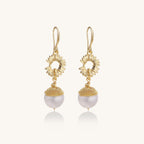 Gold-plated sunburst flower earrings with baroque pearl drops and textured metal caps on neutral background.