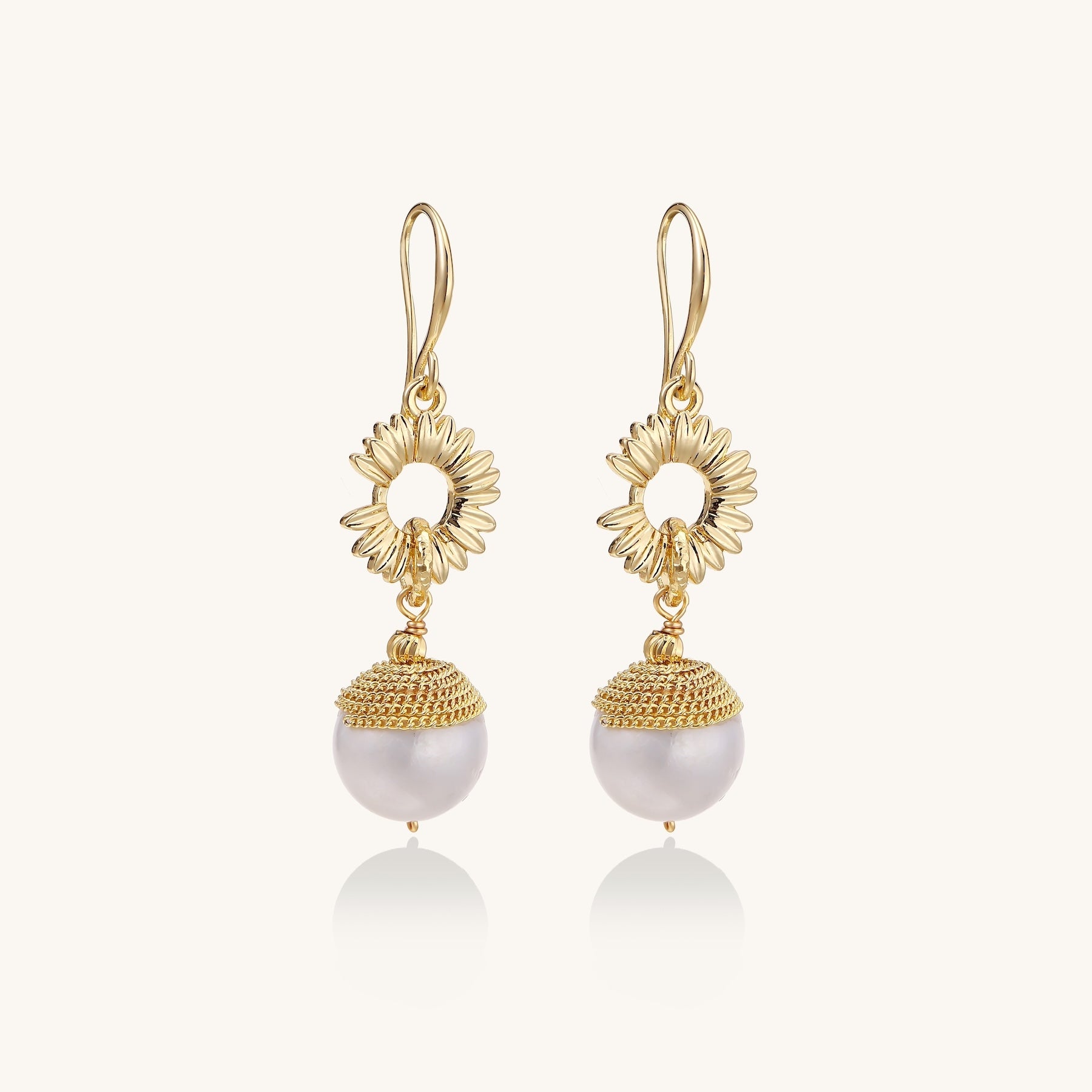 Gold-plated sunburst flower earrings with baroque pearl drops and textured metal caps on neutral background.