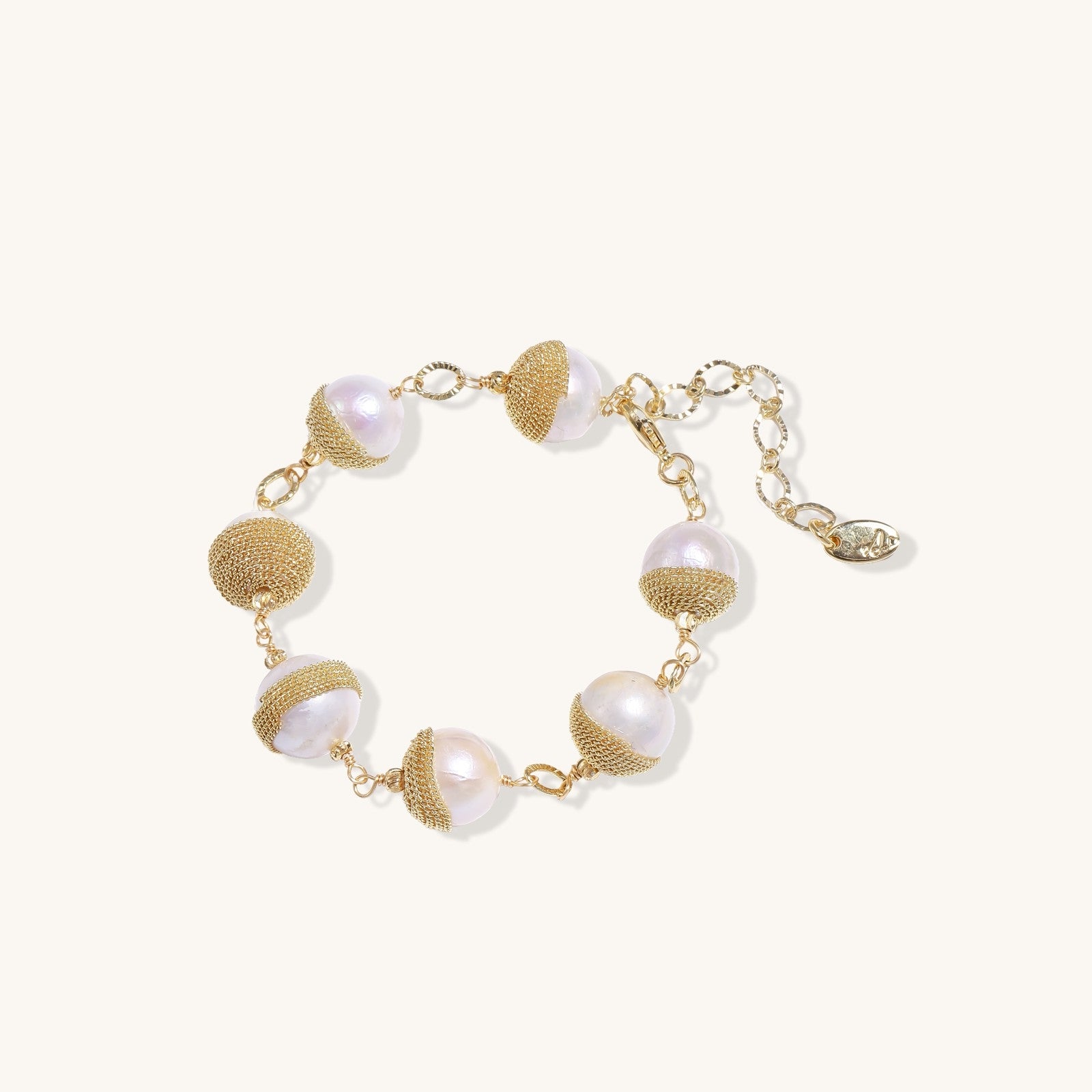 Adjustable bracelet featuring baroque pearls wrapped in gold mesh wire with delicate chain links on cream background.