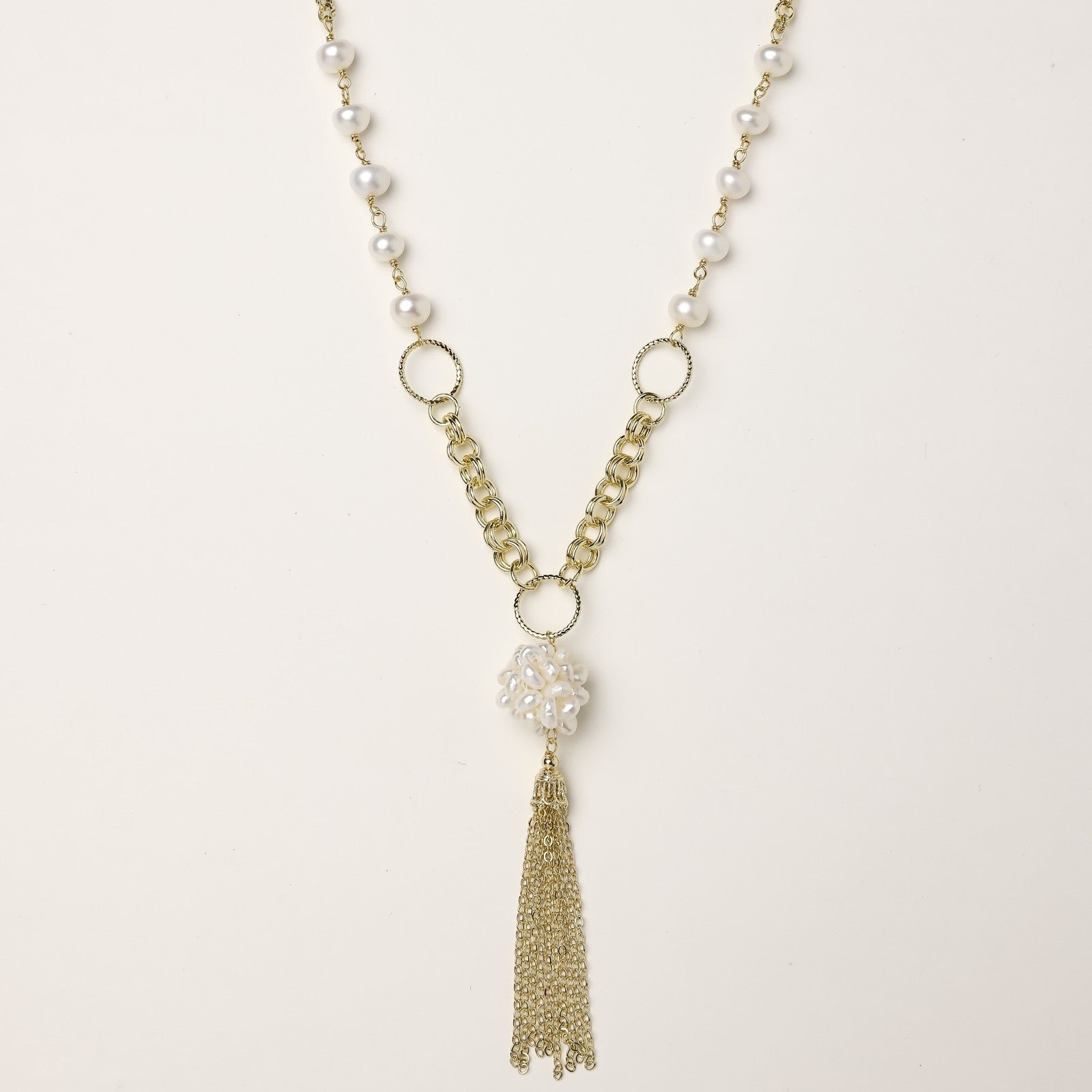 Layered gold-plated necklace with freshwater pearls, central pearl cluster, and chain tassel on cream background.