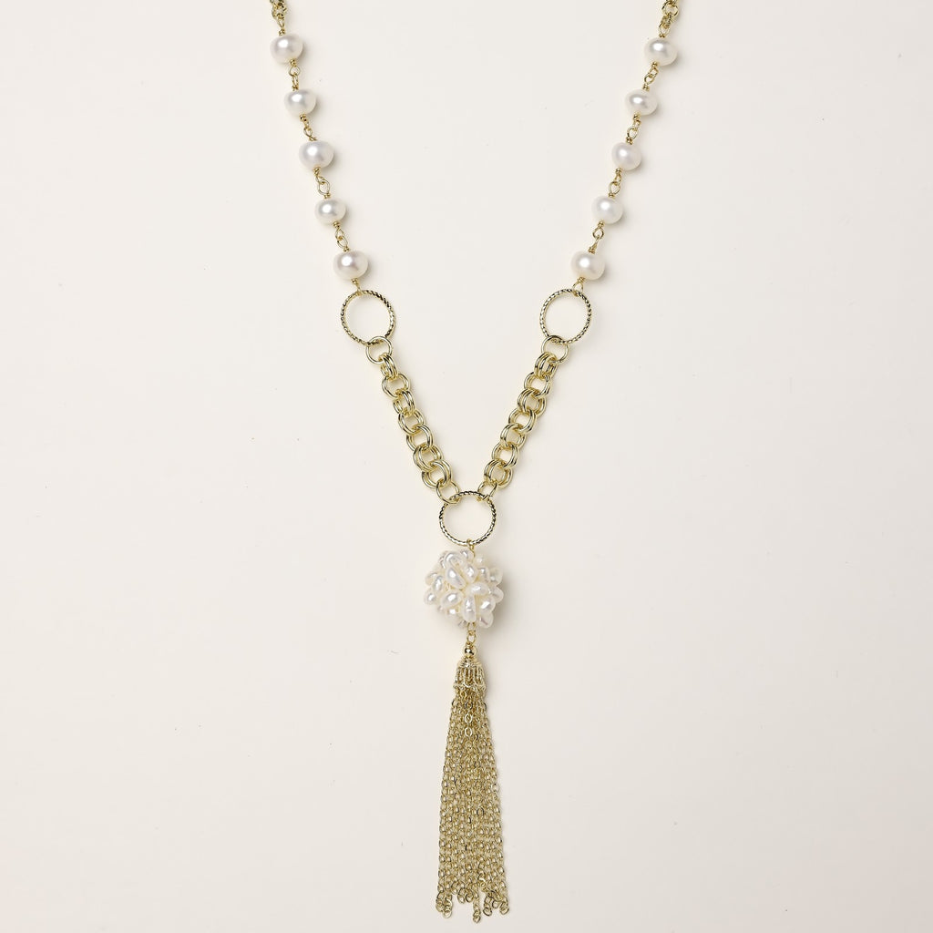 Layered gold-plated necklace with freshwater pearls, central pearl cluster, and chain tassel on cream background.