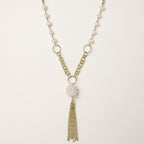 Layered gold-plated necklace with freshwater pearls, central pearl cluster, and chain tassel on cream background.