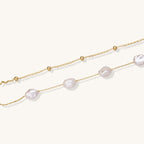 Delicate multi-layered gold-plated bracelet with irregular baroque pearls and freshwater pearls on cream background.
