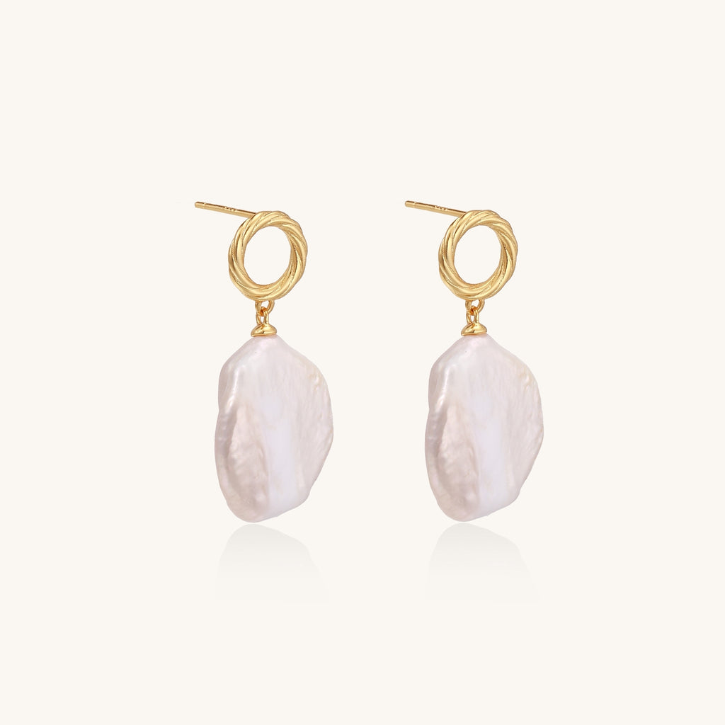 Gold-plated twisted stud earrings with large blush baroque pearls hanging elegantly on white background.