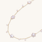 Delicate gold chain necklace with star-shaped baroque pearls and small freshwater pearls on cream background.