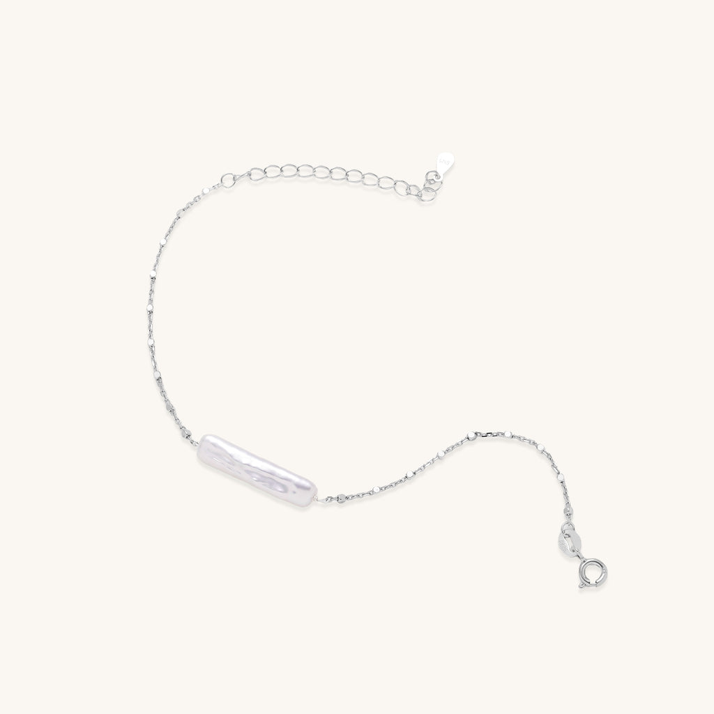 Delicate sterling silver chain bracelet with an organic white baroque pearl centerpiece on neutral background