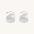 Close-up of chunky sterling silver huggie hoops with brushed matte finish against cream background.