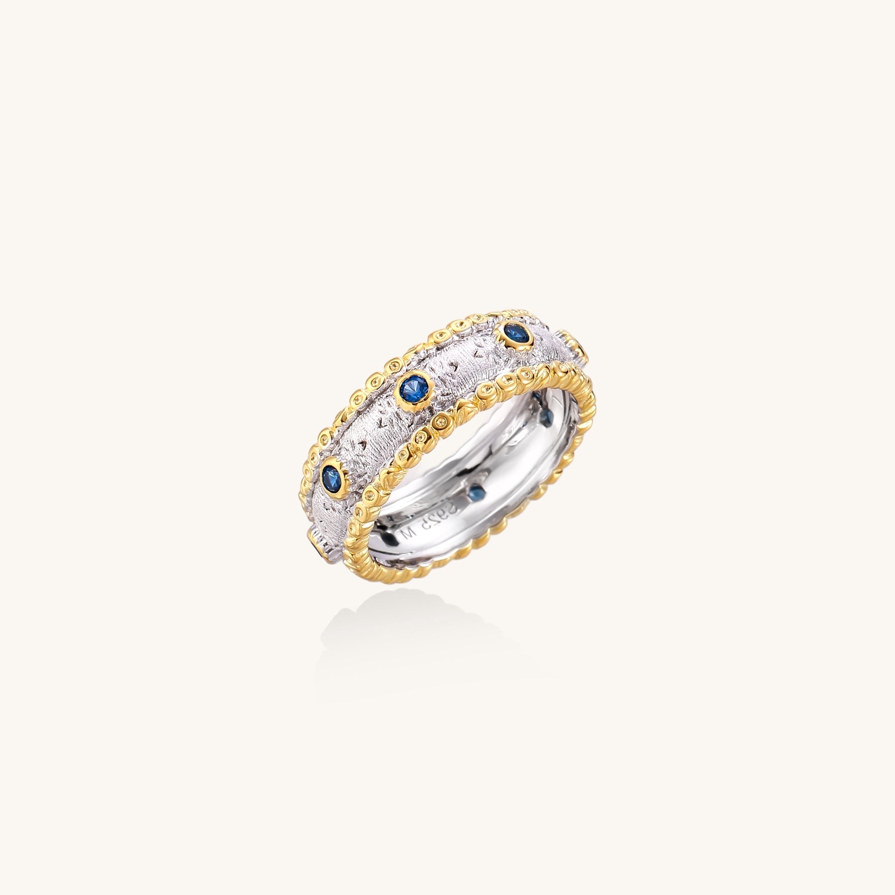 Sterling silver ring with brushed center band, blue zirconia stones, and 24k gold-plated decorative borders.