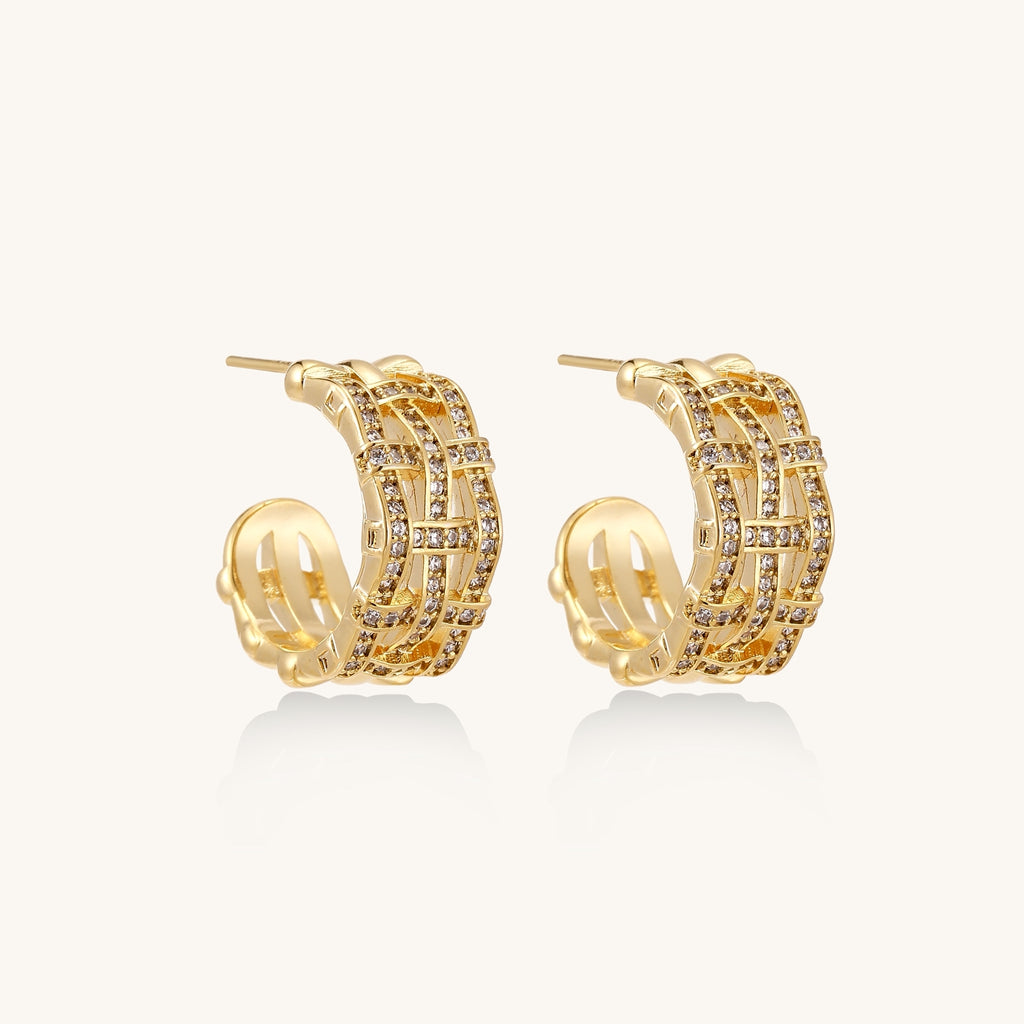 Close-up of geometric gold-plated hoop earrings with crystal pave in intricate lattice pattern on neutral background.
