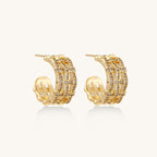 Close-up of geometric gold-plated hoop earrings with crystal pave in intricate lattice pattern on neutral background.