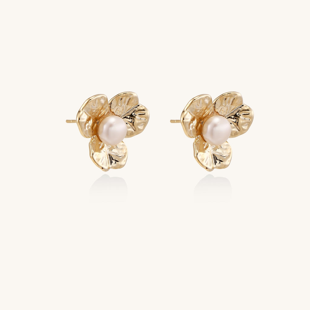 Gold-plated flower stud earrings with freshwater pearl centers on beige background, showing textured petal details.