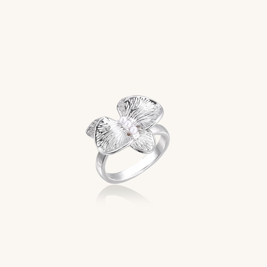 Gold-plated brass ring with textured orchid petals, zirconia stones, and center pearls on white background.