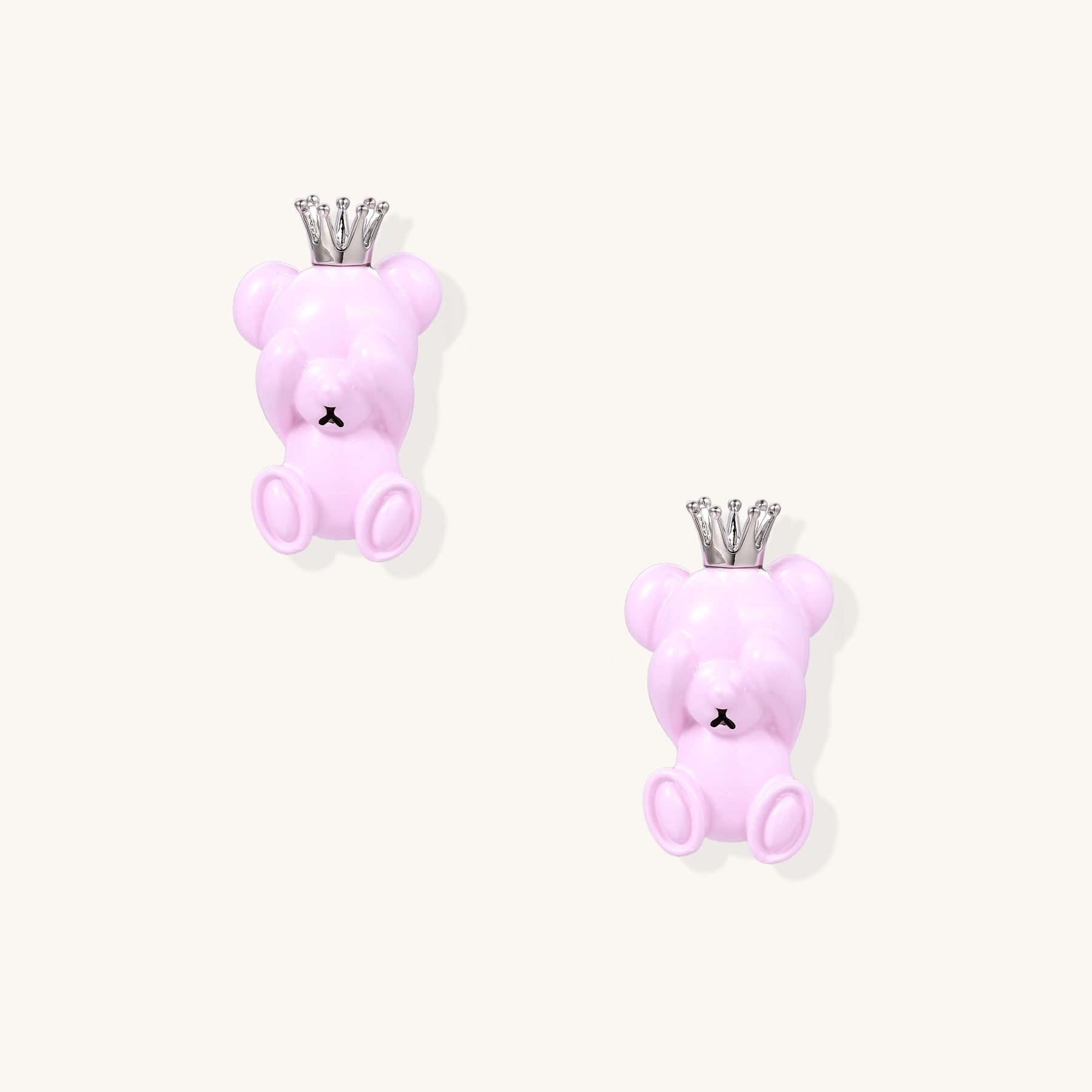 Pair of pink teddy bear-shaped stud earrings with silver crowns on white background, made from gold-plated brass