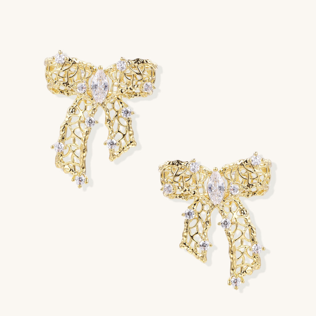 Gold and silver bow-shaped earrings with intricate lattice pattern and clear zirconia stones on neutral background.