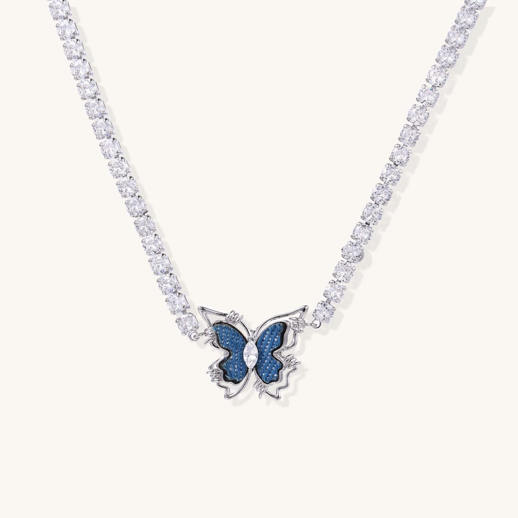 Gold-plated tennis chain necklace with blue denim butterfly pendant and zirconia stones on light background.