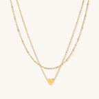Two-layer gold-plated stainless steel necklace with small heart pendant displayed on beige background
