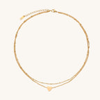 Two-layer gold-plated stainless steel necklace with small heart pendant displayed on beige background
