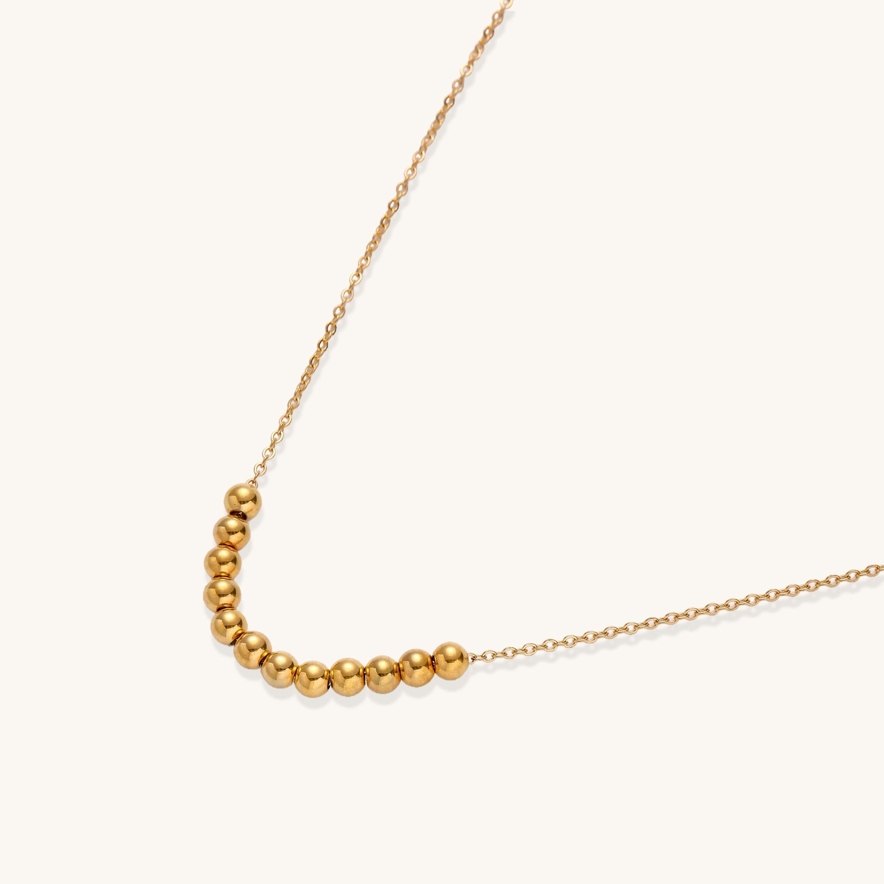 Delicate gold-plated chain necklace featuring clustered spherical beads arranged in elegant curve against white background.