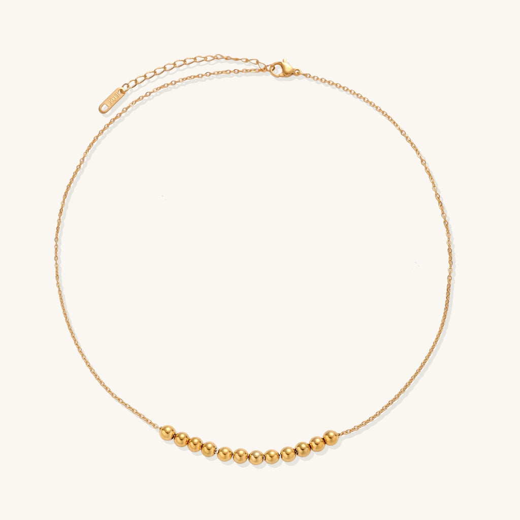 Delicate gold-plated chain necklace featuring clustered spherical beads arranged in elegant curve against white background.