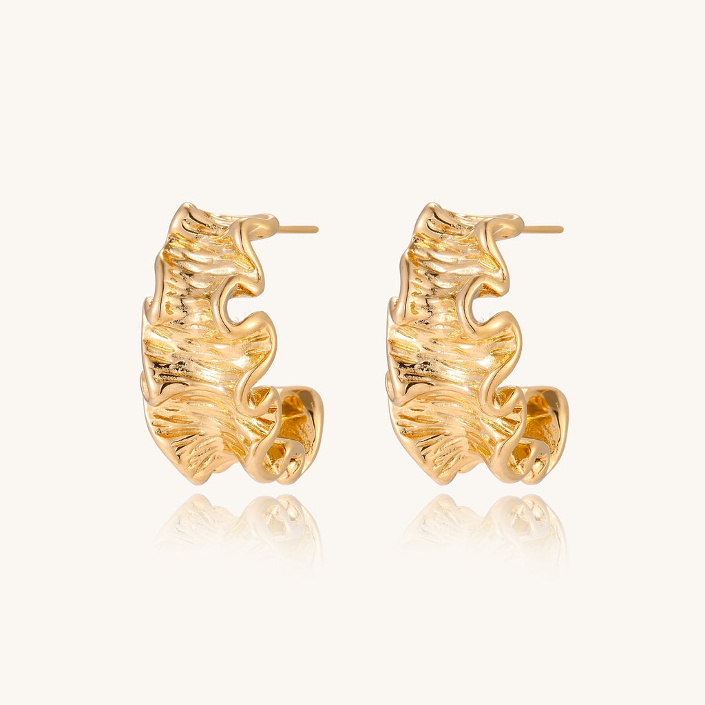 Close-up of dimensional gold-plated hoop earrings with rippled wave texture against white background.