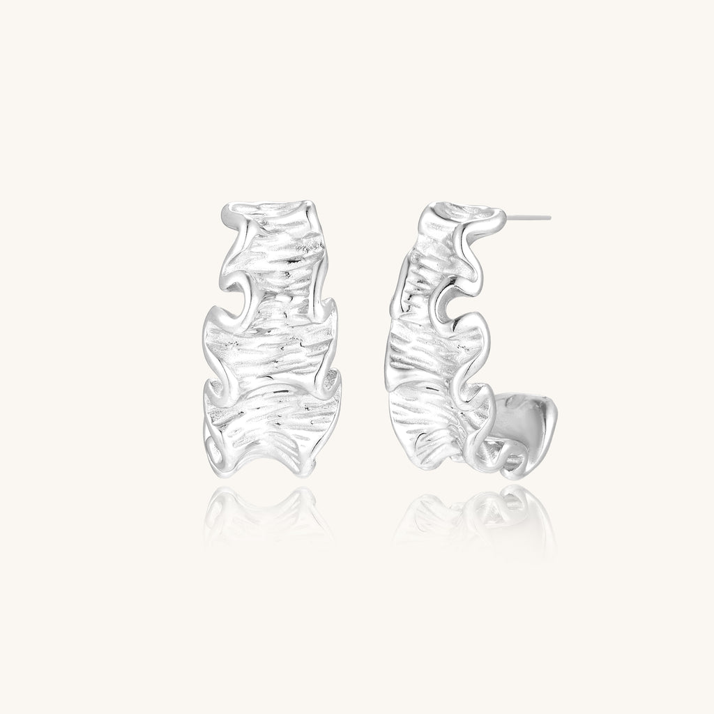 Textured gold-plated hoop earrings with flowing ripple design displayed on clean white background.