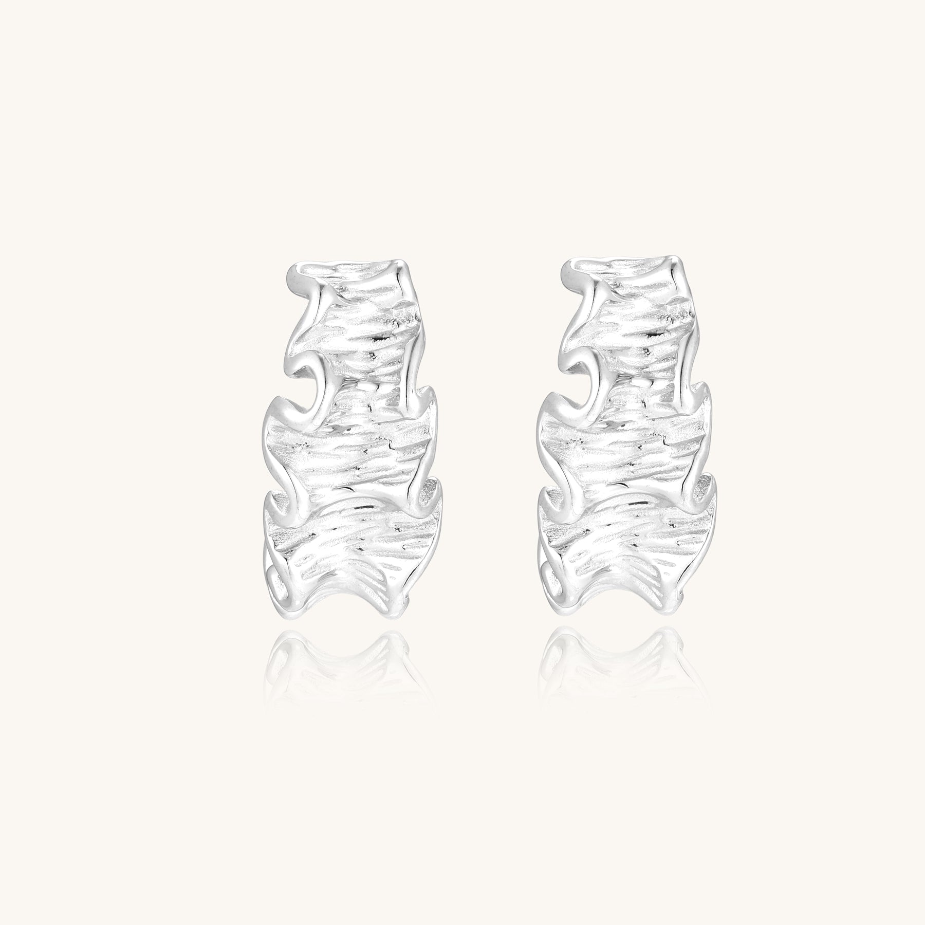 Textured gold-plated hoop earrings with flowing ripple design displayed on clean white background.