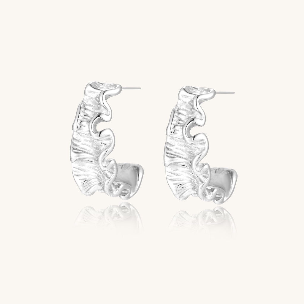 Textured gold-plated hoop earrings with flowing ripple design displayed on clean white background.