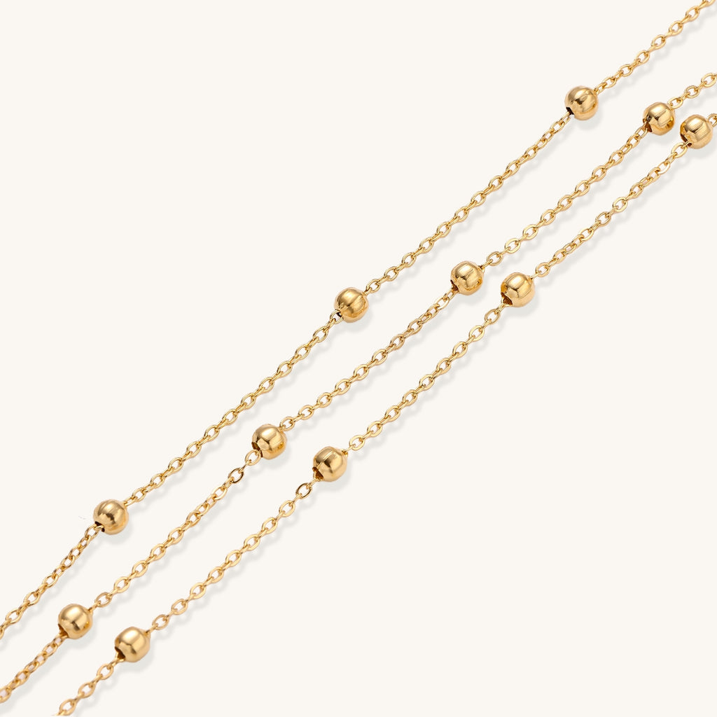 Delicate 18K gold plated bracelet with spherical beads on layered chains and adjustable extender on white background