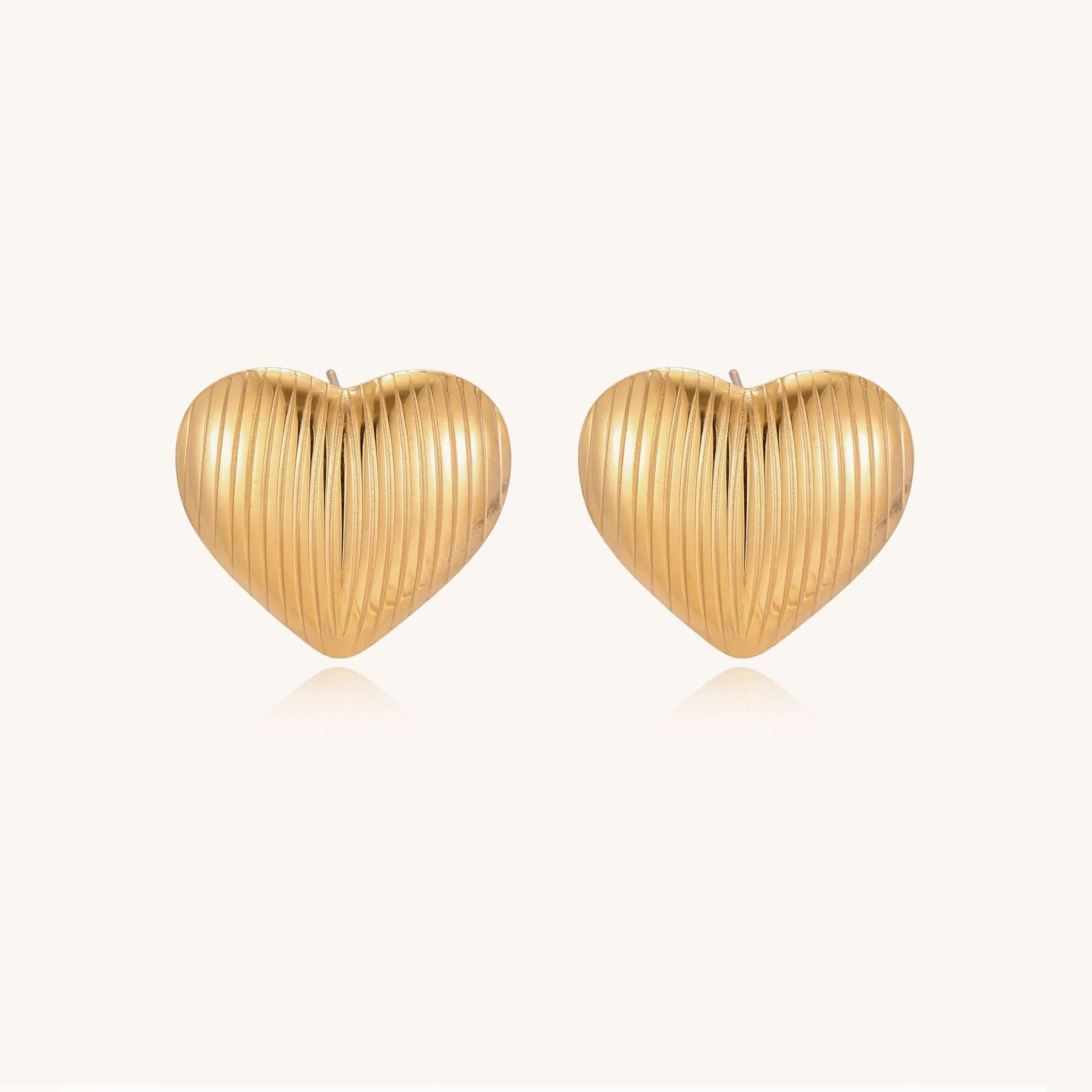 Close-up of ridged heart-shaped gold-plated stud earrings with textured surface pattern on cream background.