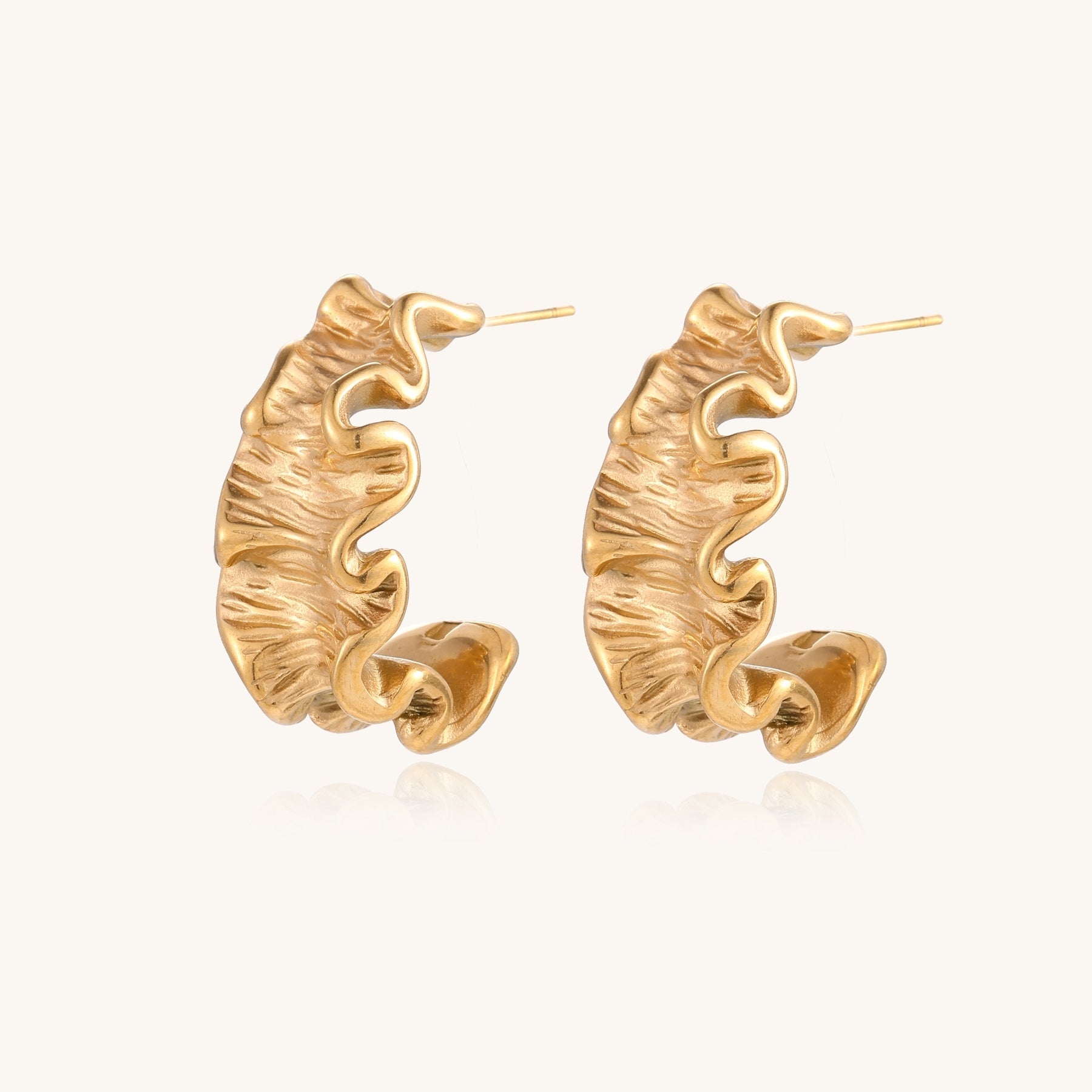Textured gold-plated hoop earrings with wavy sculptural ridges displayed against a neutral background.