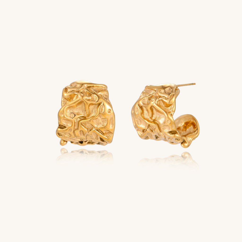 Textured gold-plated hoop earrings with organic molten surface pattern on cream background, showing intricate flowing details.