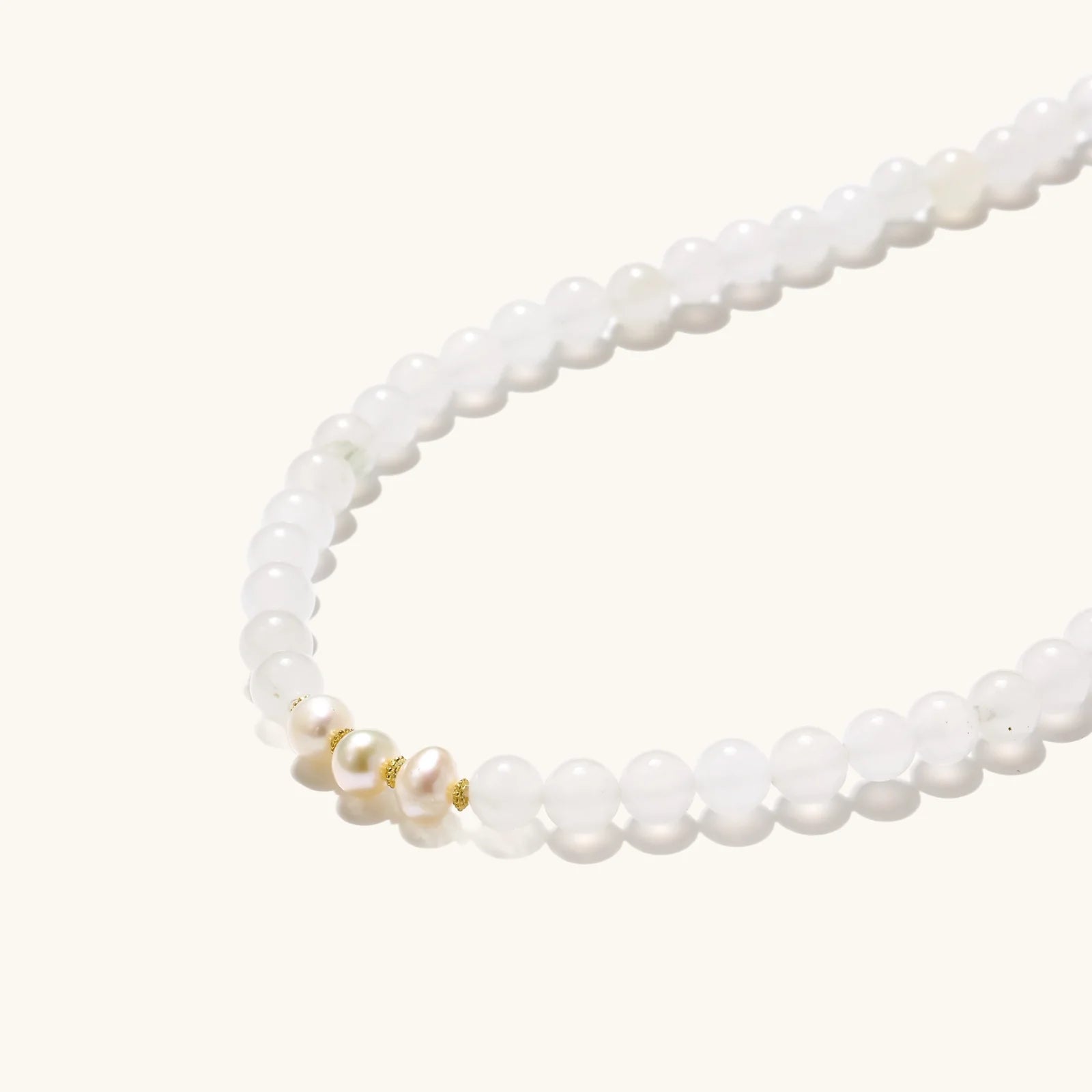 Three layered white beaded bracelets with carved orange agate lotus centerpiece and freshwater pearls on cream background.