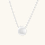 Minimalist brushed sterling silver dome pendant on delicate chain against cream background, showing matte textured finish