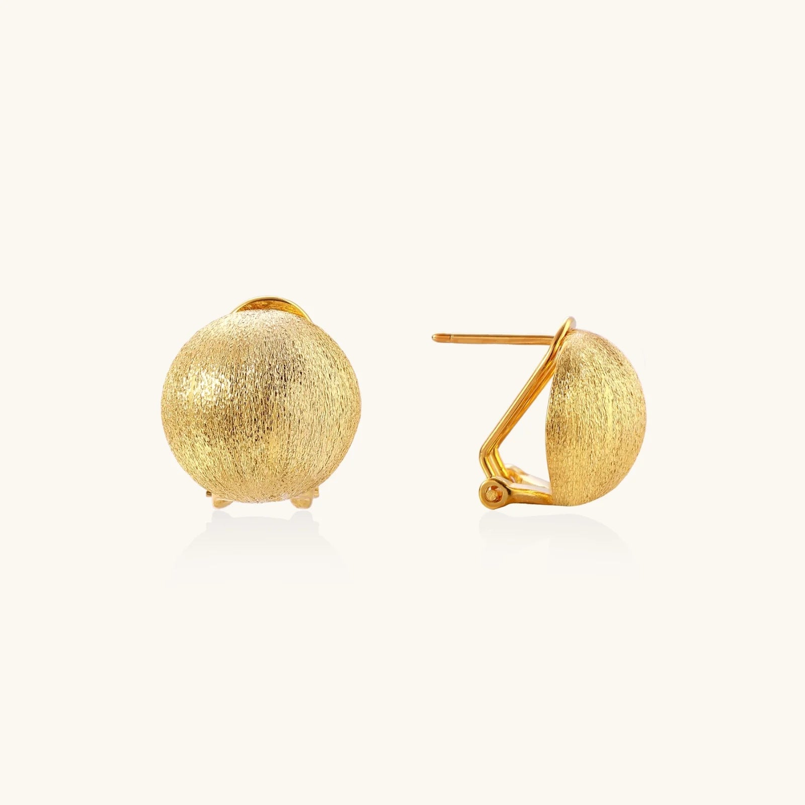 Pair of brushed gold dome earrings with clip backs showing textured matte finish on cream background